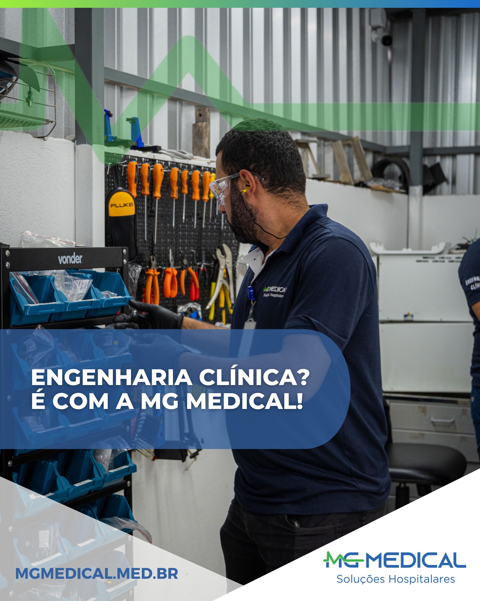 A imagem mostra um profissional técnico da área de engenharia clínica trabalhando em uma bancada organizada com ferramentas de manutenção. Ele utiliza equipamentos de proteção, como óculos de segurança e luvas, enquanto manipula peças e componentes técnicos armazenados em gavetas azuis. Ao fundo, há um painel com diversas ferramentas penduradas, como chaves de fenda e alicates, indicando um ambiente de manutenção especializado em equipamentos médicos. O profissional veste uma camisa com o logotipo da MG Medical Soluções Hospitalares. Sobre a imagem aparece um destaque gráfico com o texto: “Engenharia Clínica? É com a MG Medical!”, além do endereço do site da empresa. A cena transmite a ideia de assistência técnica especializada, organização e suporte profissional em engenharia clínica para hospitais e clínicas.